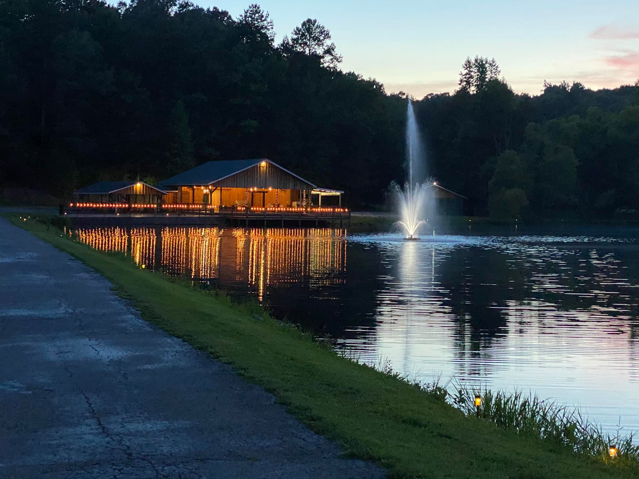 fountain in the middle of lake outside lit up wedding pavilion